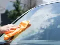 Ręka z pomarańczową ściereczką czyści szybę, pokazując, jak usunąć naklejkę z szyby.