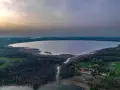 Rozległe jezioro Tuchlin otoczone lasem, z widocznym budynkiem i drogą. Zachód słońca maluje niebo.