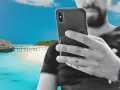 Mężczyzna z telefonem na plaży na Zanzibarze, sprawdzający zanzibar internet. W tle turkusowa woda i drewniany pomost.