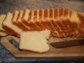 Tranches de pâte à pain de mie dorées et moelleuses, prêtes à être dégustées sur une planche en bois avec un couteau.