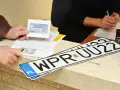 Nowe rejestracje samochodowe w urzędzie. Klient pokazuje dokumenty, a na ladzie leżą tablice rejestracyjne.