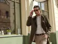 Mężczyzna w eleganckim płaszczu w kolorze khaki, który to kolor jest idealny na wiosenne dni, poprawia okulary przeciwsłoneczne.