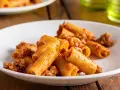 Rigatoni conditi con un ricco ragù di salsiccia, serviti su un piatto bianco.