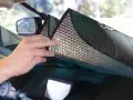 Mani che posizionano un parasole riflettente sul cruscotto per proteggere l'auto dal sole.