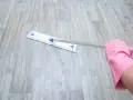 Mano con guante rosa limpiando suelo vinílico con mopa.
