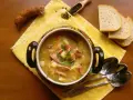 Aromaticzny kapuśniak z kiełbasą i ziemniakami, podany w ozdobnym naczyniu, obok kromek chleba i ziaren pieprzu.