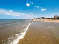 Onda che lambisce la sabbia dorata, con ombrelloni e palazzi sullo sfondo. Un classico scenario di **Emilia Romagna mare**.