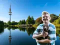 Mann mit Dackel genießt Hamburg umsonst am Wasser, Fernsehturm im Hintergrund.