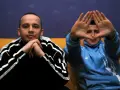 Dwóch mężczyzn w dresach, jeden z rękami złożonymi na brodzie, drugi tworzy rękami kształt serca. Klimat hip hop i rap.