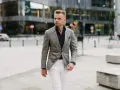 Elegancki mężczyzna w szarej marynarce w kratę i białych spodniach. Idealne połączenie, jeśli zastanawiasz się, jakie spodnie do szarej marynarki pasują.