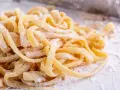 Świeży makaron jajeczny, lekko oprószony mąką, czeka na gotowanie. W porównaniu do makaronu ziarnistego, ten jest gładki i delikatny.