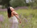 Portrait en bokeh d'une femme aux yeux fermés, bras croisés sur la poitrine, dans un champ de fleurs sauvages mauves.