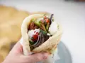 En hand håller en gyros med kött, grönsaker och vit sås. Perfekt för supergod fredagsmat!