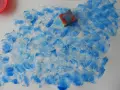 Peinture à l'éponge sur toile, créant un effet de vagues bleues et blanches. Une éponge est posée sur la toile.