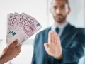 Ręka podaje plik banknotów 500 euro. Mężczyzna w garniturze odrzuca ofertę, mówiąc, że klient nie zapłacił za usługę.