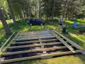 En kvinna förbereder sig för att skruva trall på en nybyggd altan i en lummig trädgård.