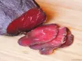 Bresaola co to? Ciemnoczerwone, cienko pokrojone plastry suszonej wołowiny na desce.
