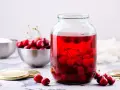 Duży słoik wypełniony rubinowym kompotem z wiśni, obok miska świeżych owoców i cukru.