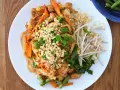 Pyszny sos pad thai z kurczakiem, warzywami i orzeszkami ziemnymi, podany z kiełkami fasoli mung.