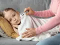 Dziecko leży pod kocem, a mama mierzy mu temperaturę. Wysoka gorączka u dziecka bez innych objawów martwi.
