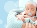 Śpiące dziecko z chupkiem, kiedy smoczek jest za mały, otulone kocykiem.