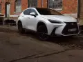 Biały Lexus 350h z czarnymi felgami stoi przed starą ceglaną budowką.