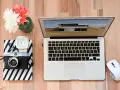 Jak zgrać zdjęcia z aparatu na laptop? Na biurku leży aparat, laptop i myszka.