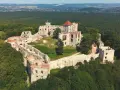 Ruiny zamku Tenczyn na wzgórzu, otoczone lasem. Widać mury obronne, wieże i pozostałości budynków.