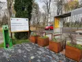 Zielona stacja serwisowa dla rowerów i tablica informacyjna o projekcie VeloMetropolis w Małopolsce. W tle czerwony samochód i jesienne drzewa.