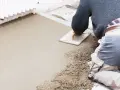 Operaio al lavoro con una cazzuola, livella il cemento per aumentare l'altezza del pavimento.
