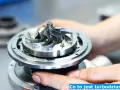 Zbliżenie na turbosprężarkę samochodową, którą trzymają dłonie mechanika.