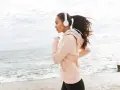 Kobieta w słuchawkach biega nad morzem, ciesząc się ćwiczeniami cardio.