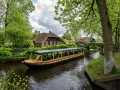 Bootfahrt durch Giethoorn, das Venedig der Niederlande. Grüne Ufer, Reetdachhäuser und gelbe Blumen am Wasser.