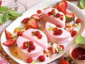 Delizioso semifreddo alle fragole, guarnito con fragoline di bosco, salsa rossa e foglioline verdi.