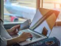 Osoba z paszportem i biletem czeka na lotnisku, sprawdzając na laptopie, ile czasu na odbiór paszportu.
