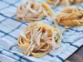 Świeże, domowe tagliatelle lub makaron spaghetti ułożone na lnianym ręczniku w kratkę.