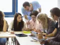 Des étudiants travaillent en groupe, un enseignant les supervise. Ils préparent leur diplôme BAFD, concentrés sur leurs notes et tablettes.