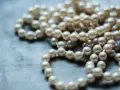 Collana di perle su sfondo grigio. Scopri come pulire la madreperla per mantenerla splendente.