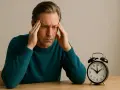 Uomo con le mani sulle tempie, espressione di stanchezza mentale. Accanto, una sveglia analogica.