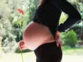 Brzuszek w 3 miesiącu ciąży, delikatnie podtrzymywany dłonią, z kwiatkiem w tle.