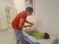 Lekarz bada chłopca leżącego na kozetce, oceniając objawy uszkodzonego układu nerwowego u dziecka.