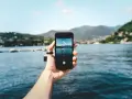 Dłoń trzyma smartfon, na ekranie którego widać zdjęcie jeziora z łódką. To przykład techniki photo stacking, która pozwala uzyskać niezwykłą głębię ostrości.