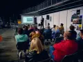 Prezentacja na targach budowlanych. Mężczyzna przemawia do zgromadzonej publiczności, która siedzi na krzesłach.