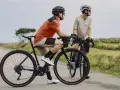 Dwóch rowerzystów na szosie, jeden w pomarańczowej koszulce, drugi w beżowej. To idealny widok na to, co to gravel - wszechstronność i przygoda.