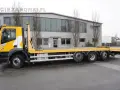Żółty Iveco Stralis z platformą transportową stoi przed budynkiem.