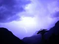 Un éclair zèbre le ciel violet d'un **orage en montagne que faire** ? Une cabine de téléphérique silhouette se dresse, témoin de la fureur de la nature.