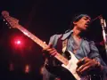 Jimi Hendrix, einer der besten Gitarristen, spielt auf der Bühne seine weiße Fender Stratocaster. Rotes Licht beleuchtet die Szene.