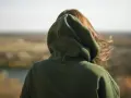 Osoba w zielonej bluzie z kapturem patrzy na krajobraz. Nie wiadomo, ile waży bluza z kapturem, ale wygląda na ciepłą.