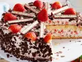 Eine köstliche Yogurette Torte mit frischen Erdbeeren, Schokostückchen und Sahne. Ein Stück ist bereits angeschnitten.