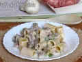 Piatto di pasta alla boscaiola con funghi, piselli e salsiccia, servita su un piatto bianco con una tovaglietta di juta.